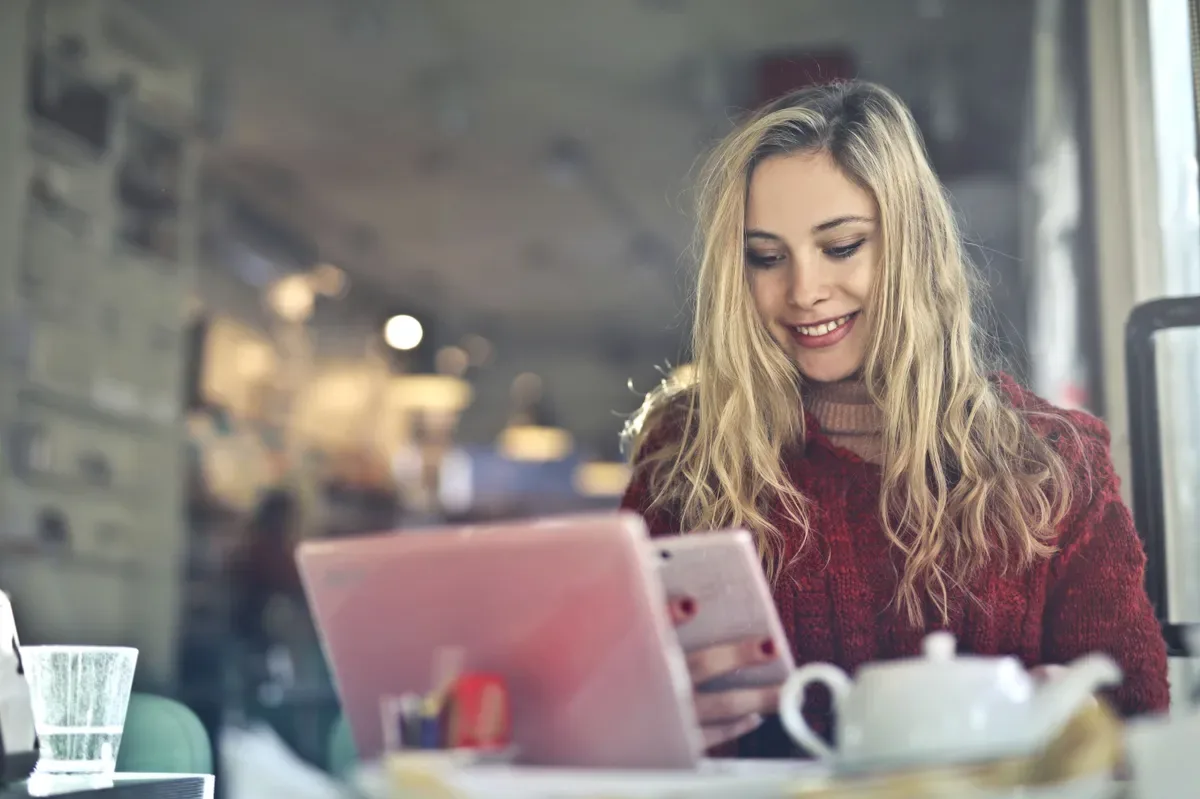 Jovem usando celular e notebook em um café, ilustrando a busca por relacionamento sugar em plataforma verificada