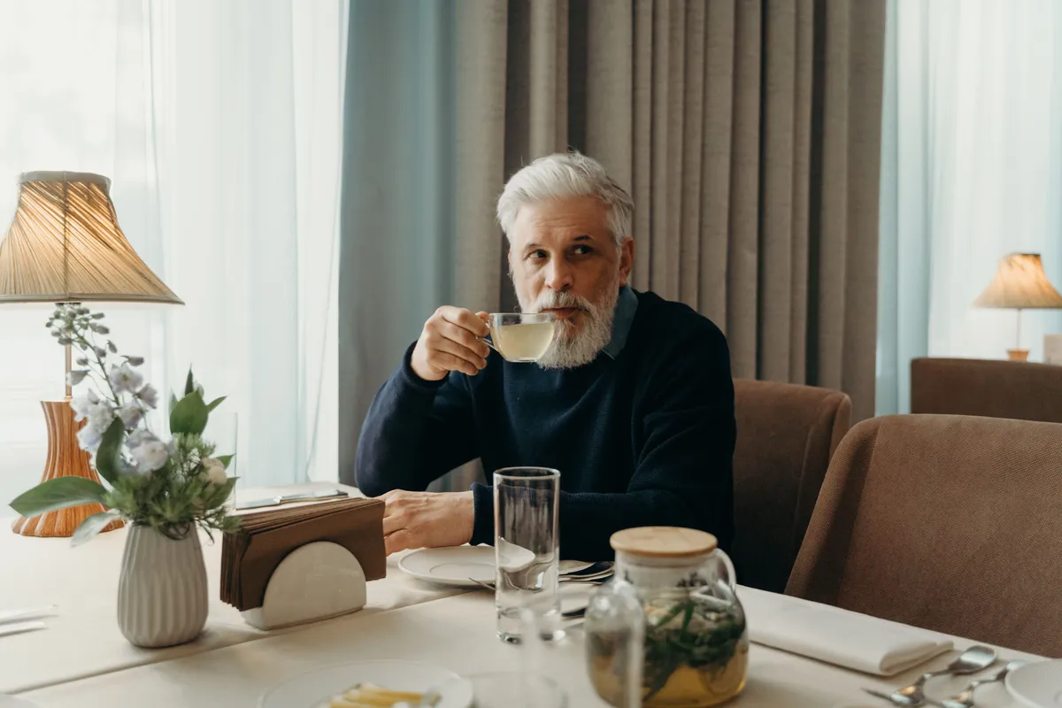Homem grisalho e elegante tomando chá num restaurante, ilustrando como conhecer homens com mais de 60 anos
