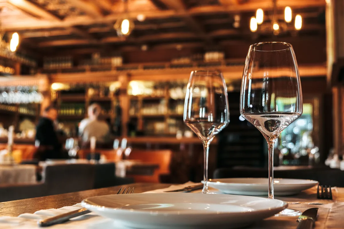 Mesa posta para dois em restaurante movimentado, com taças e pratos, cenário de um primeiro encontro em lugar público