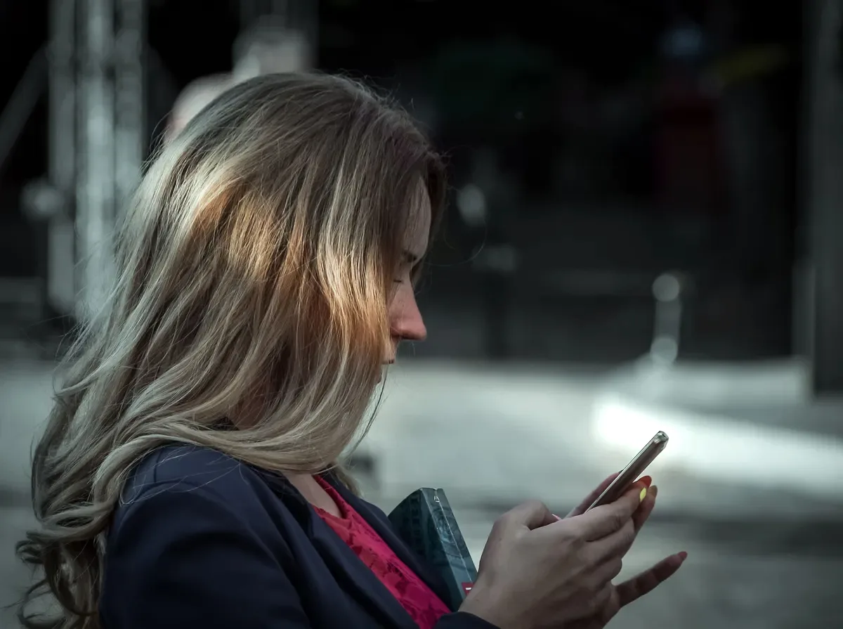 Mulher olhando o celular com atenção na rua, ilustrando cuidados de segurança em relacionamento sugar