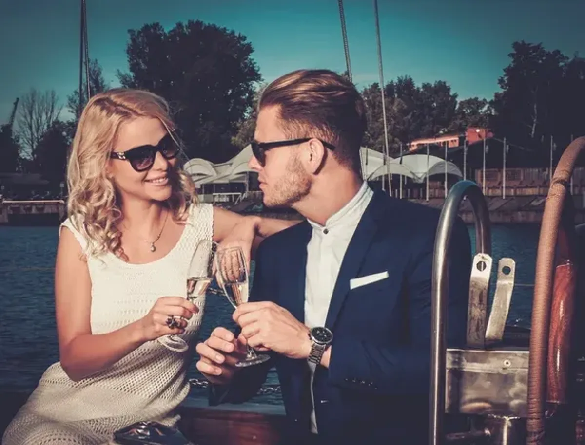 Casal em barco brindando com champanhe, ilustrando relacionamento com apoio financeiro em site de velho rico