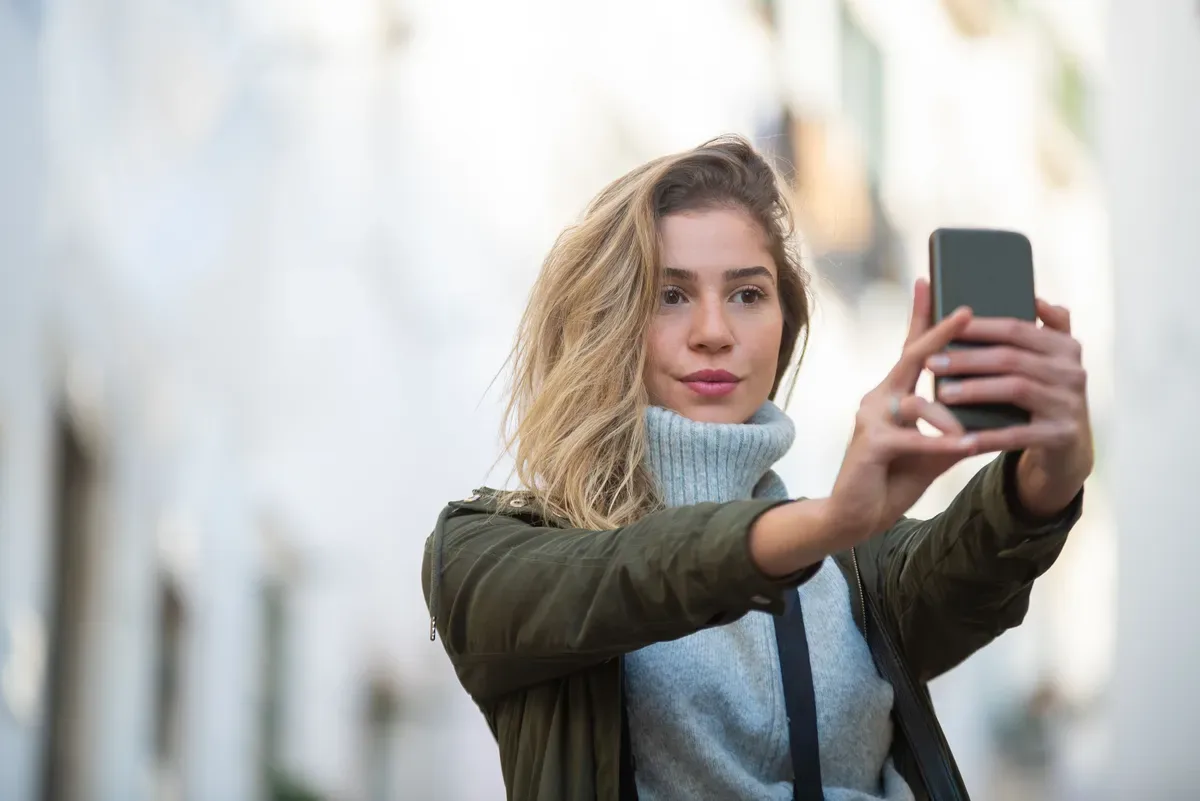 Jovem segurando o celular à frente do rosto, ilustrando chamada de vídeo em relacionamento sugar virtual